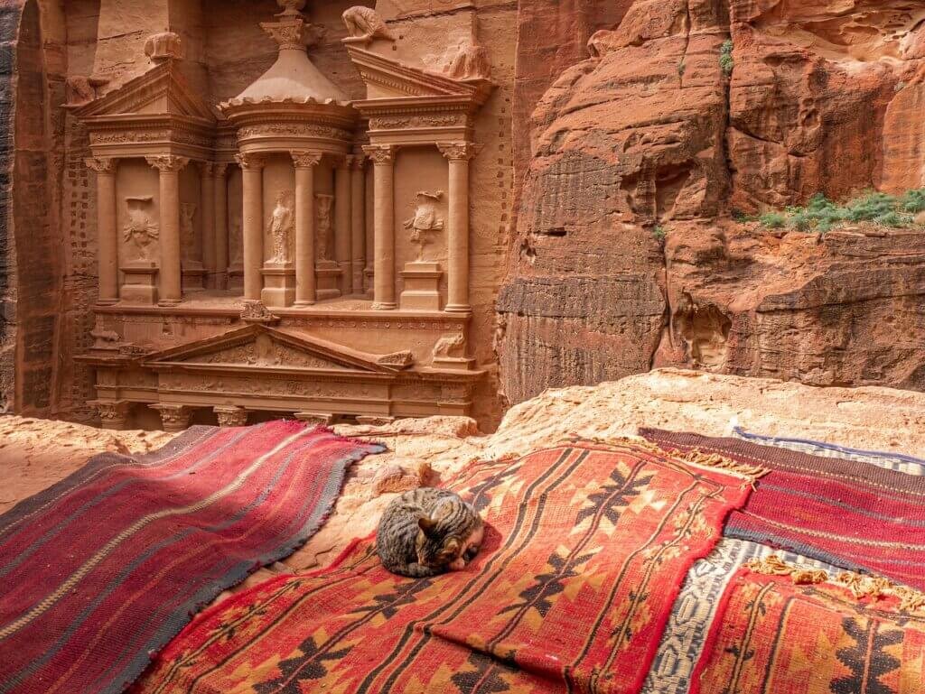 The Treasury in Petra, Jordan, an iconic historical landmark, with vibrant Bedouin carpets in the foreground and rocky sandstone cliffs.