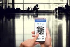 Hand holding a smartphone displaying a mobile boarding pass at an airport, representing the convenience of budget airlines.