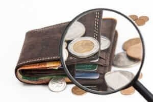 Close-up of a magnifying glass over a wallet with coins and bills, representing hidden fees when booking cheap flights.